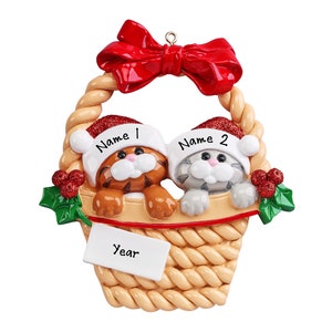 May include: A Christmas ornament featuring two kittens wearing Santa hats in a basket with a red bow. The basket has a tag that says "Year" and the kittens have name tags that say "Name 1" and "Name 2".