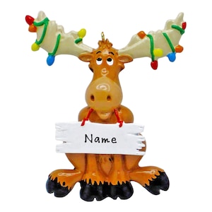 May include: A brown moose Christmas ornament with a white sign that says "Name". The moose has a string of colorful lights wrapped around its antlers.