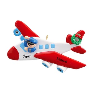 May include: A white and red airplane ornament with a pilot figure in the cockpit. The ornament has a small green wreath with a red bow on the tail. The word "Year" is printed on the front.