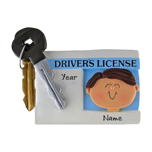 May include: A novelty ornament shaped like a driver's license with a car key attached. The license has a blue background with a cartoon face and the words "DRIVER'S LICENSE", "Year", and "Name". The key is black and silver.