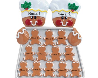 May include: A Christmas ornament featuring two gingerbread chefs wearing white hats with holly accents. They hold a tray of gingerbread men cookies, each labeled with a name. The ornament is brown, white, red, and silver.