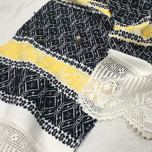 Puede incluir: Una tela blanca con patrones geométricos negros y amarillos. La tela tiene un borde de ganchillo blanco.