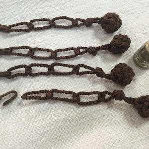 Peut inclure: Quatre fermetures en cordon et glands marrons avec des boucles métalliques. Un dé à coudre argenté est également présent sur l'image.