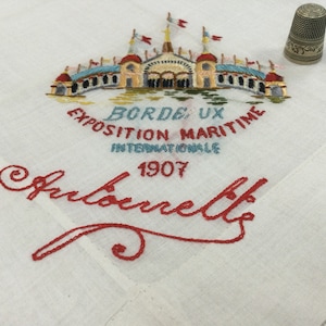 May include: White linen handkerchief with red embroidery of a building with the text "Bordeaux Exposition Maritime Internationale 1907" and the signature "Suberette".