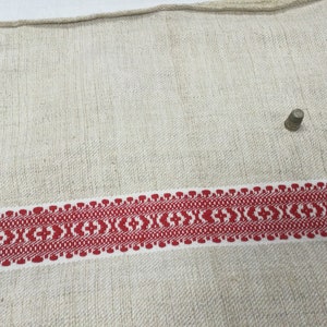 May include: A white linen fabric with a red woven border. A small silver thimble is sitting on the fabric.