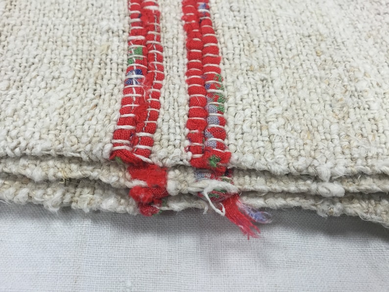 May include: Close-up of a white woven rug with two red stripes along the edge. The rug is folded in thirds, showing the layers of the weave.