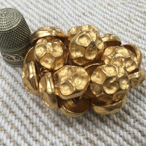 Könnte beinhalten: Eine Ansammlung goldfarbener Metallknöpfe mit einer strukturierten, unebenen Oberfläche. Die Knöpfe sind kreisförmig angeordnet und scheinen vintage zu sein.