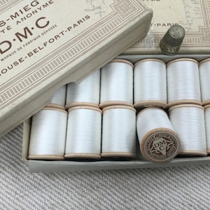 Könnte beinhalten: Eine Schachtel mit weißen DMC-Stickgarnrollen mit dem Text "OLLFUS-MIEG SOCIÉTÉ ANONYME D.M.C MARQUE DE FABRIQUE DÉPOSÉE MULHOUSE-BELFORT-PARIS" auf der Schachtel.