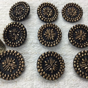 May include: Twelve round black buttons with gold accents and a raised design. The buttons have a shiny finish.
