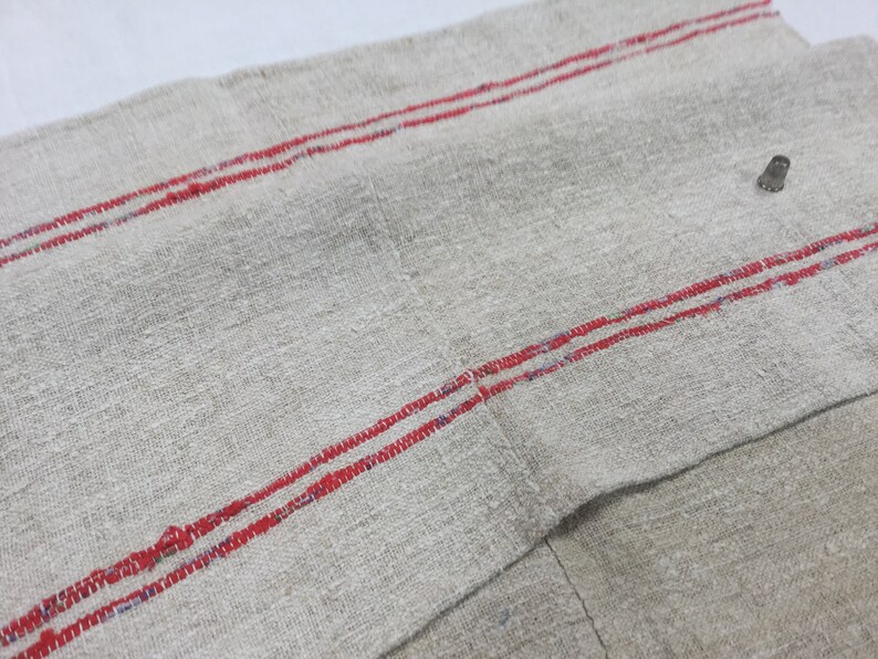 May include: A piece of off-white linen fabric with two red stripes running horizontally across the fabric.