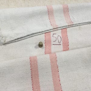 May include: White fabric with two pink stripes and the number "50" written in black ink.