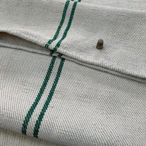 May include: A white linen fabric with two green stripes running vertically. The fabric is folded over, showing the texture of the weave.