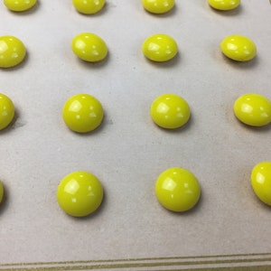 May include: A sheet of paper with 15 yellow buttons arranged in a grid pattern.