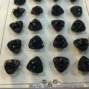 May include: A card of 18 black triangle-shaped buttons with a star design. The card reads "Made in Czechoslovakia".