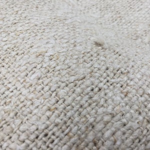 May include: Close-up of a woven fabric with a natural, off-white color. The fabric has a rough texture and a tight weave.
