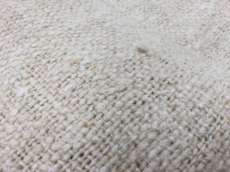 May include: Close-up of a woven fabric with a natural, off-white color. The fabric has a rough texture and a tight weave.