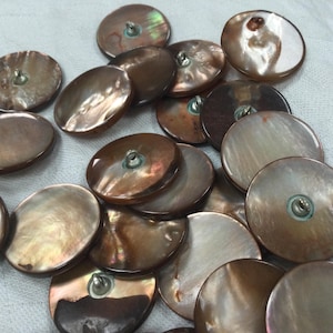 May include: A selection of iridescent, round buttons in shades of brown and tan. Each button has a metal shank for sewing. The buttons vary in size and have a pearlescent sheen, reflecting light.