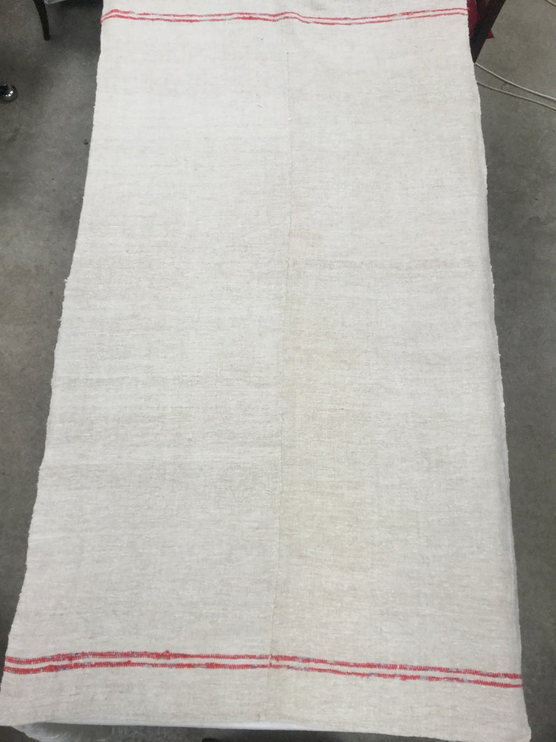 May include: A large, off-white linen tablecloth with two thin red stripes along the top and bottom edges.