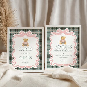 May include: Two framed signs with a plaid background and pink accents. One sign reads "CARDS and GIFTS thank you" and the other says "FAVORS please take one thank you for celebrating with us today - Lauren-". Each sign features a teddy bear illustration.