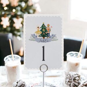 May include: A light blue table number card with a scalloped edge, featuring a festive illustration of a ballerina, Christmas tree, and nutcracker. The word "Table" is written on a banner, with the number "1" below.