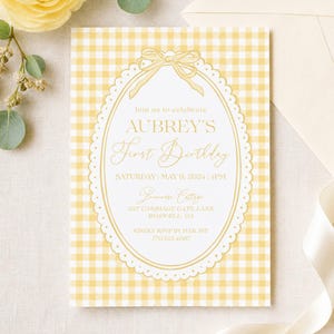 May include: A yellow and white gingham patterned invitation for Aubrey's first birthday. The invitation features an oval frame with a bow at the top and the text "Join us to celebrate AUBREY'S First Birthday". The date, time, and location are also included.