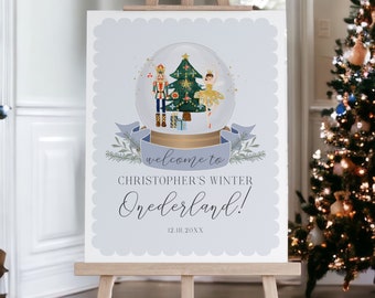 May include: A light blue welcome sign on an easel. The sign features a snow globe illustration with a Christmas tree, nutcracker, and ballerina. Text reads "welcome to Christopher's Winter Onederland!" and a date. The sign has a scalloped border.