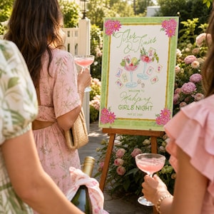 May include: A wooden easel displaying a sign with the words "Tiles & Tinies" and "Welcome to Mahjong Girls Night", with cocktail and playing card illustrations. People are holding cocktails and a champagne bottle.