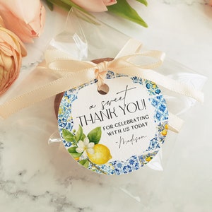 May include: A white round thank you tag with blue and yellow floral design. The tag says "a sweet thank you! for celebrating with us today - Madison".