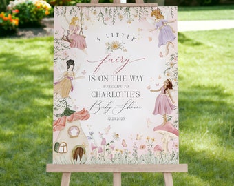 Pode incluir: Um cavalete de madeira exibe uma placa de chá de bebê com tema de fadas. A placa apresenta ilustrações de fadas, flores e uma casa de cogumelos. O texto diz "A Little Fairy Is On The Way" e dá as boas-vindas aos convidados.