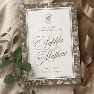 May include: A rectangular wedding welcome sign featuring a white center panel with the text Welcome to the wedding of Sophia & Mathew, May 27, 2029, Roswell, Georgia, surrounded by a dark taupe border with a detailed white floral botanical pattern.