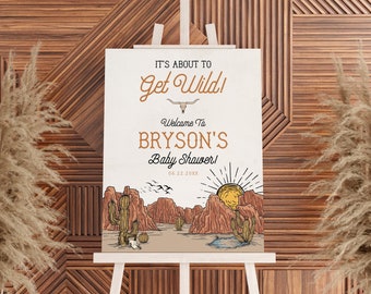 May include: A white sign with brown text that reads "It's about to Get Wild! Welcome to Bryson's Baby Shower! 06.22.20XX". The sign features a cartoon illustration of a desert landscape with cacti, mountains, and a sunset.