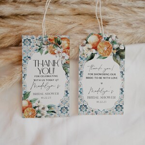 Könnte beinhalten: Zwei dekorative Geschenkanhänger mit floralen und Zitrusdesigns. Die Anhänger tragen den Text "Danke!" und "Bridal Shower" mit einem Datum. Die Anhänger sind rechteckig mit abgerundeten Oberteilen und mit einer Schnur gebunden.