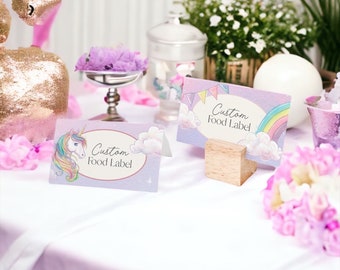 May include: Two rectangular paper food labels with a light purple background. One label features a colorful unicorn illustration, while the other displays a rainbow and bunting flags. Both cards have an oval center with the text Custom Food Label.