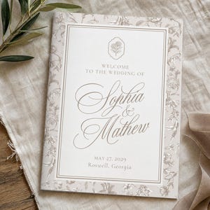 May include: A rectangular wedding programme booklet with a beige floral border. The centre features the text Welcome to the wedding of Sophia & Mathew, May 27, 2029, Roswell, Georgia, and a small floral icon in a decorative frame.