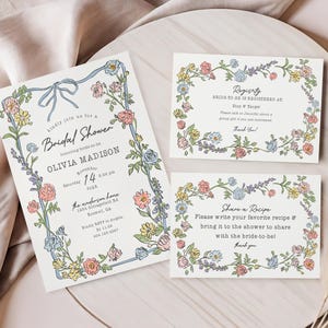 Może przedstawiać: Zaproszenia i karty na baby shower z kwiatowymi obramowaniami. Gł&oacute;wne zaproszenie zawiera niebieską wstążkę i tekst, w tym imię panny młodej i szczeg&oacute;ły wydarzenia. Dodatkowe karty zawierają informacje.