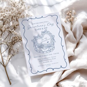 Puede incluir: Una invitación azul claro para el Día de San Valentín con un borde decorativo y un diseño de pastel en forma de corazón. La invitación incluye el texto "Join the girls for a Galentine's Day Cake & Sip" y detalles del evento.