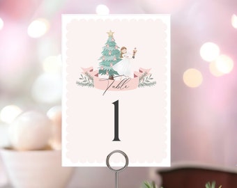 May include: A light pink table number card with a scalloped edge. The card features a Christmas tree, a ballerina, and the word "Table" above the number "1". A silver metal holder supports the card.