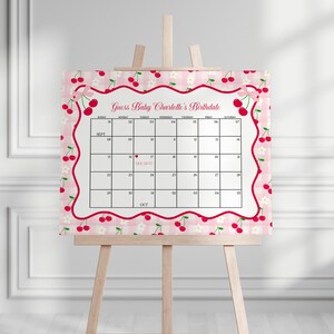 May include: A baby shower calendar on an easel. The calendar has a pink gingham background with a cherry border and the text "Guess Baby Charlotte's Birthdate." The calendar grid is for September and October.