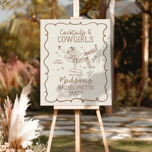 May include: A white sign with brown text and a line drawing of a cowgirl sitting in a martini glass. The sign reads "Cocktails & Cowgirls" and "Welcome to Madison's Bachelorette Party".