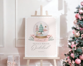 May include: A pink sign on a wooden easel with a snow globe illustration. The snow globe features a Christmas tree, a ballerina, and a nutcracker. The sign reads "Welcome to Olivia's Winter Onederland!" and the date 12.18.20XX.