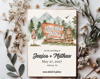Op de afbeelding: Save the Date huwelijksuitnodiging met een aquarel-illustratie van een berglandschap, een houten bord met de tekst "Save the Date" en een stenen constructie met het nummer "76" erop. De tekst onder de illustratie luidt "voor de bruiloft van Jessica + Mathew, 27 mei 2027, Atlanta, Georgia, meer details volgen."