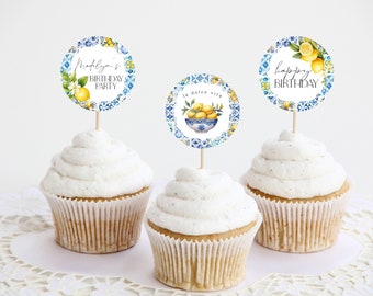 May include: Three white cupcakes with blue and white patterned cupcake toppers. The toppers feature lemons, a bowl of lemons, and the text "Madelyn's Birthday Party" and "Happy Birthday".
