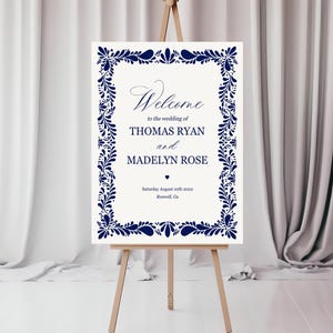 May include: A white wedding welcome sign with a navy blue floral border. The sign reads "Welcome to the wedding of Thomas Ryan and Madelyn Rose, Saturday August 10th 2002, Roswell Ga."