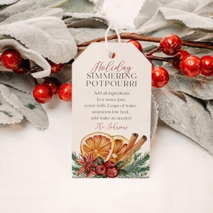 May include: A gift tag with the text "Holiday Simmering Potpourri" in red script. The tag features illustrations of dried orange slices, cinnamon sticks, cranberries, and greenery. A white string is attached to the tag.