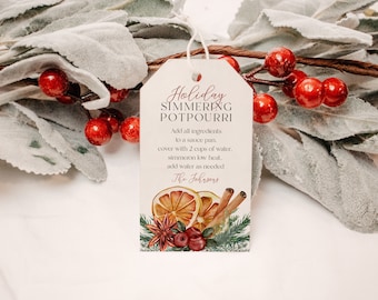 May include: A gift tag with the text "Holiday Simmering Potpourri" in red script. The tag features illustrations of dried orange slices, cinnamon sticks, cranberries, and greenery. A white string is attached to the tag.