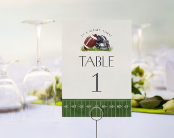 May include: A table number card with a football theme. The card features a football and helmet graphic with the text "IT'S GAME TIME!" and "TABLE 1". The bottom of the card has a green field design with yard lines.
