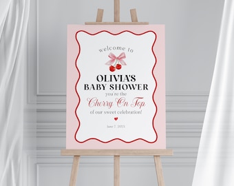 Op de afbeelding: Een roze babyborrelbord op een ezel. Het bord heeft een rode geschulpte rand en bevat de tekst "welcome to OLIVIA'S BABY SHOWER you're the Cherry On Top of our sweet celebration!" met kersenillustraties.