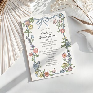 May include: A bridal shower menu with floral border. The menu features the text "LET'S EAT" and "Madison's Bridal Shower". The menu includes appetizers, entree, and dessert options. The floral border includes pink, yellow, and blue flowers.