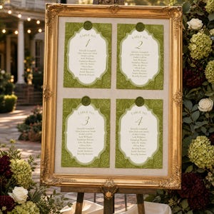 May include: A gold framed seating chart with four cards, each labeled with a table number. The cards have a green floral design and include guest names. The chart is displayed on a wooden easel, surrounded by flowers.