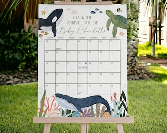 Könnte beinhalten: Ein Babyparty-Kalender auf einer Staffelei mit dem Text "Errate das Ankunftsdatum von Baby Charlotte". Der Kalender zeigt Illustrationen von Meereslebewesen, darunter ein Wal, eine Meeresschildkröte und ein Orca, mit einem Kalenderraster.